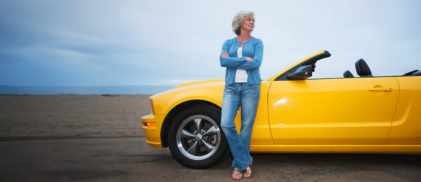 Lady leaning back on her yellow convertible parked by the beach her arms folded 