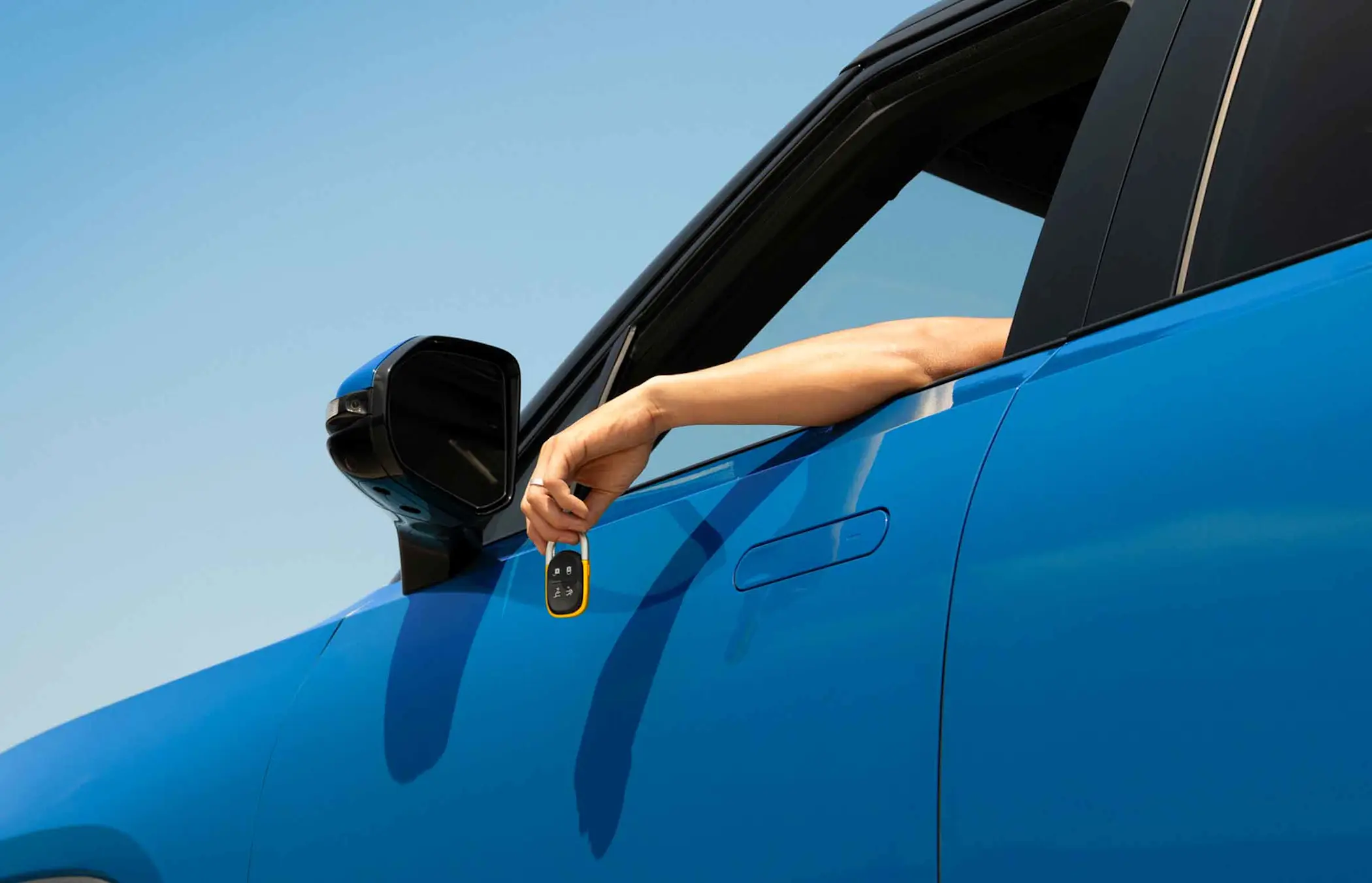 Exterior view of a blue SUV with the driver's door visible; a hand is extended out of the open window holding a car key