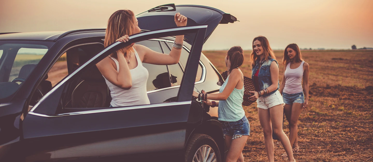 Four women unloading a picnic basket from a 7 passenger SUV in a field at dusk