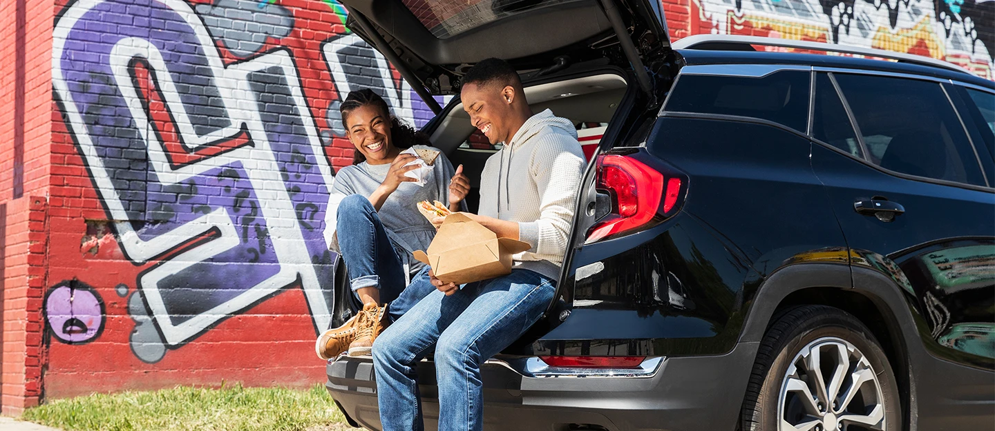 Man and woman laughing as they eat pizza and sit in the back on the SUV