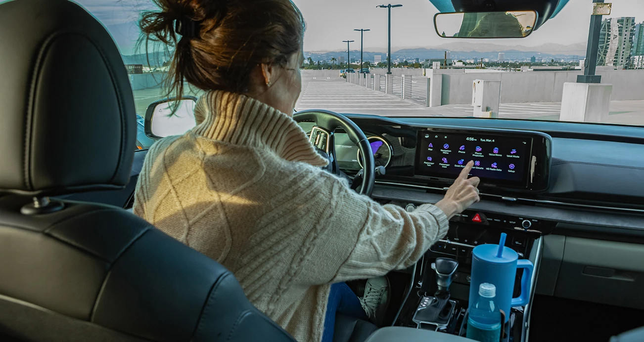 Host sitting behind wheel of a Kia Carnival making a selection on the infotainment screen