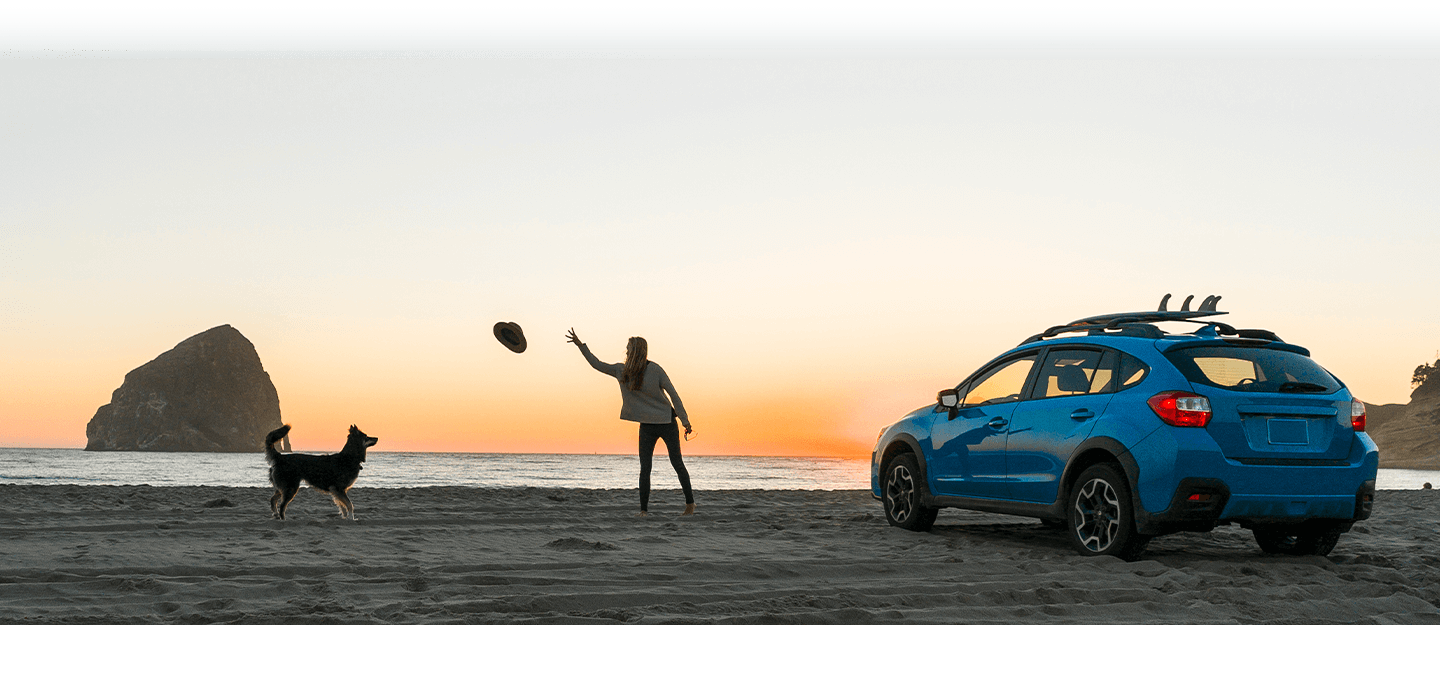 Woman and dog on beach playing frisbee at sunset blue subaru parked next to them