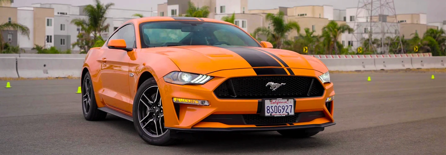 Orange Mustang with a black stripe down the middle parked in a parking lot 