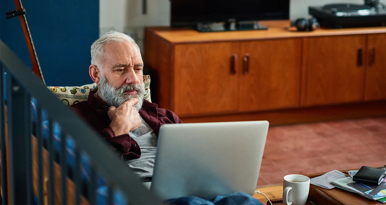 Man sitting on couch researching his cars value on his laptio while enjoying a cup of coffee