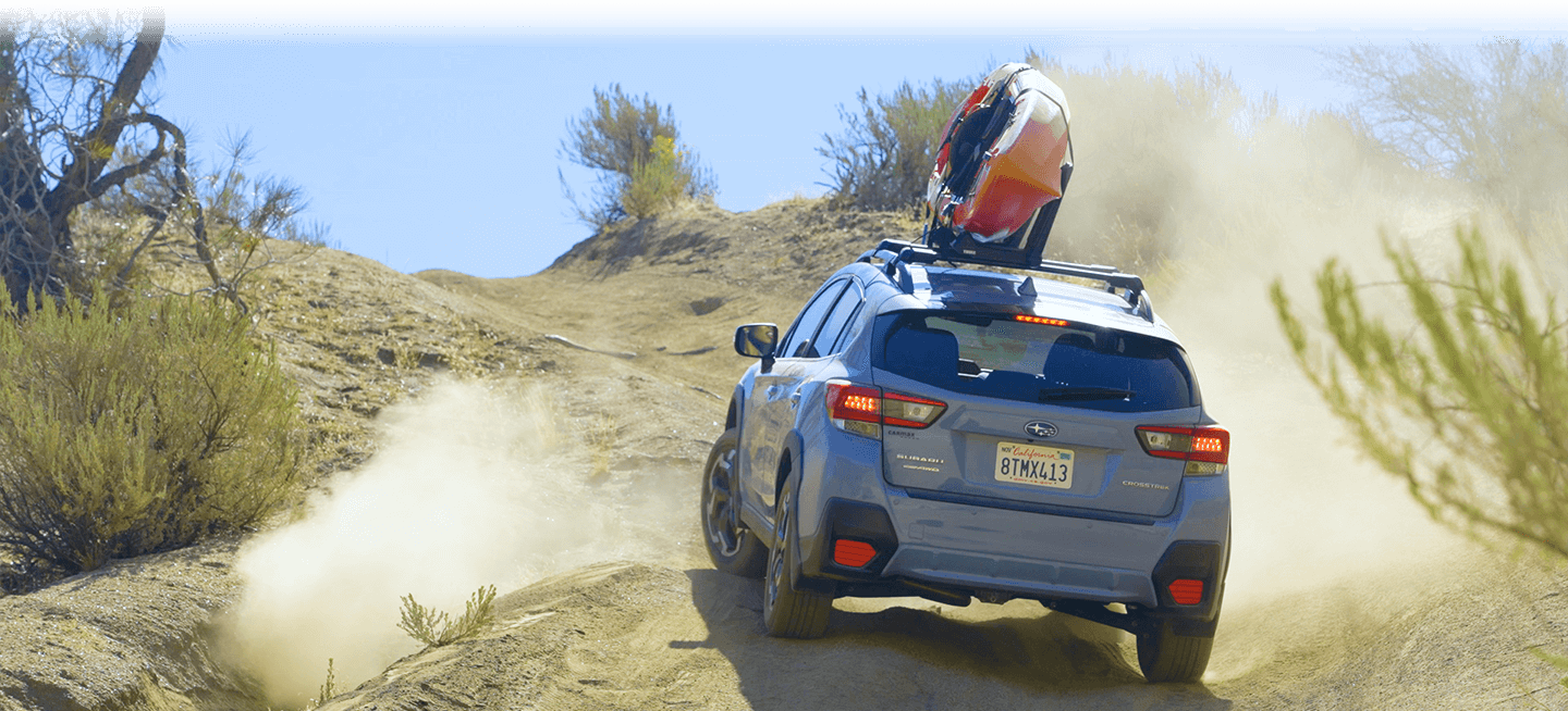 A 2022 Subaru Crosstrek in Cool-Gray Khaki off-roading on dusty hill with a orange kayak strapped down to roof racks