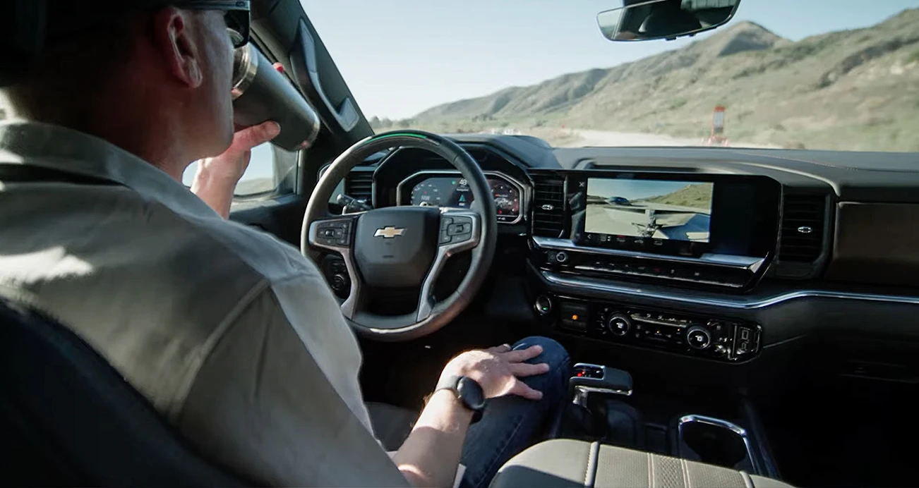 Man sitting in drivers seat taking a sip of coffee supervising his car in "self drive" mode