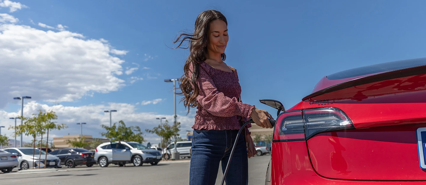 Woman plugs in her red Tesla in parking lot of charge 