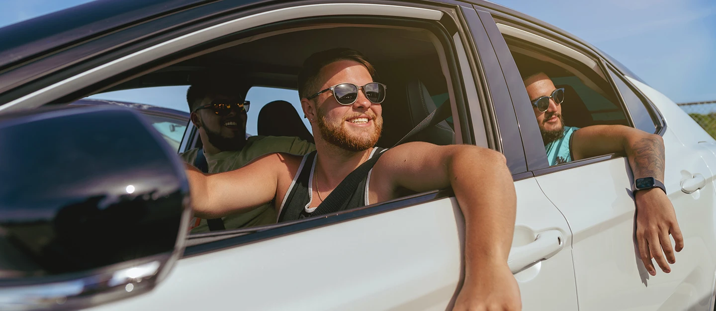 Three male friends driving with the windows down in their white sedan