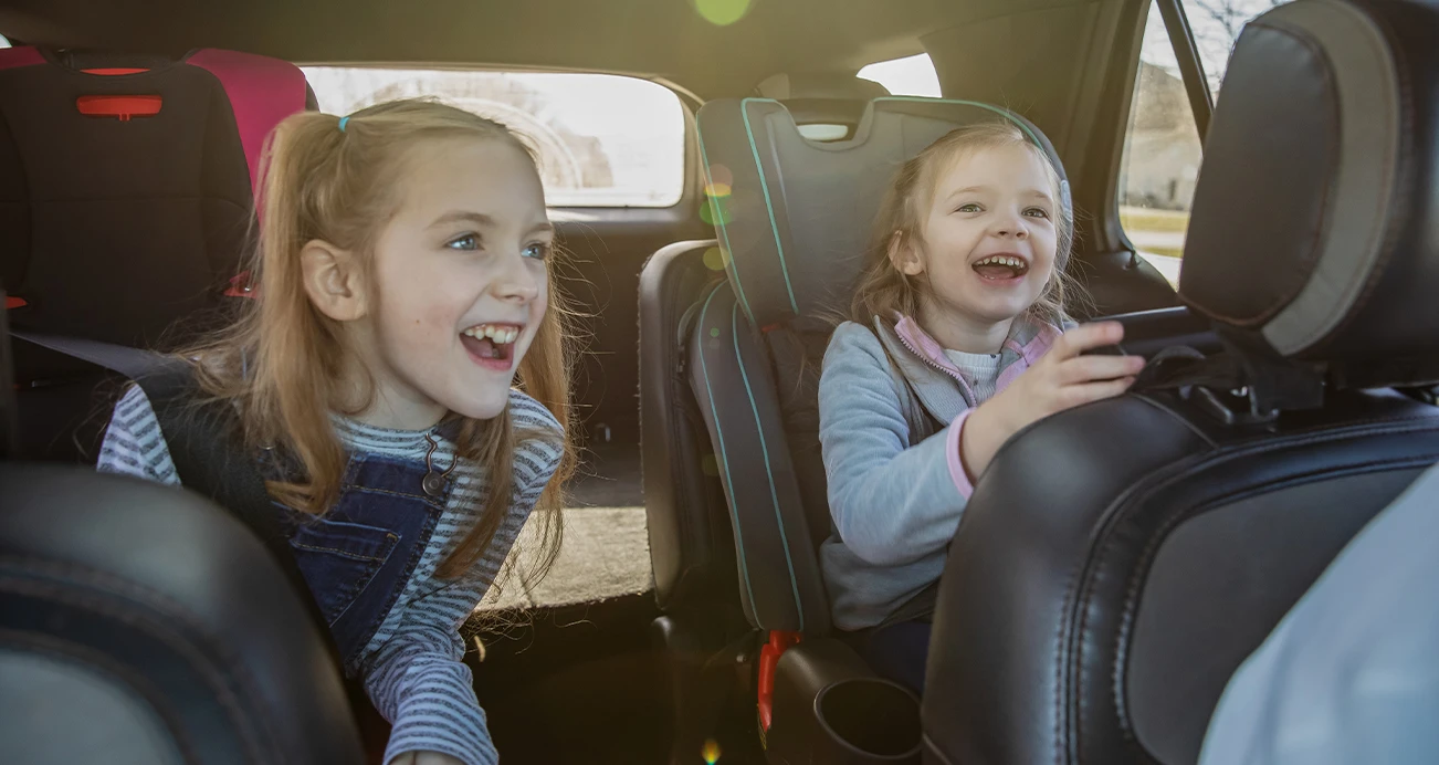 2 kids laughing while sitting in their car seats in vehicle equipped with second row captains chairs