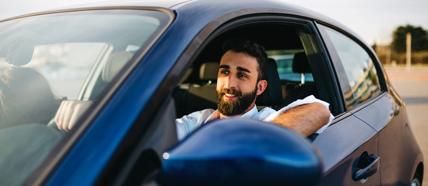 Man sitting behind the wheel of a blue coupe his arm is resting on open window 