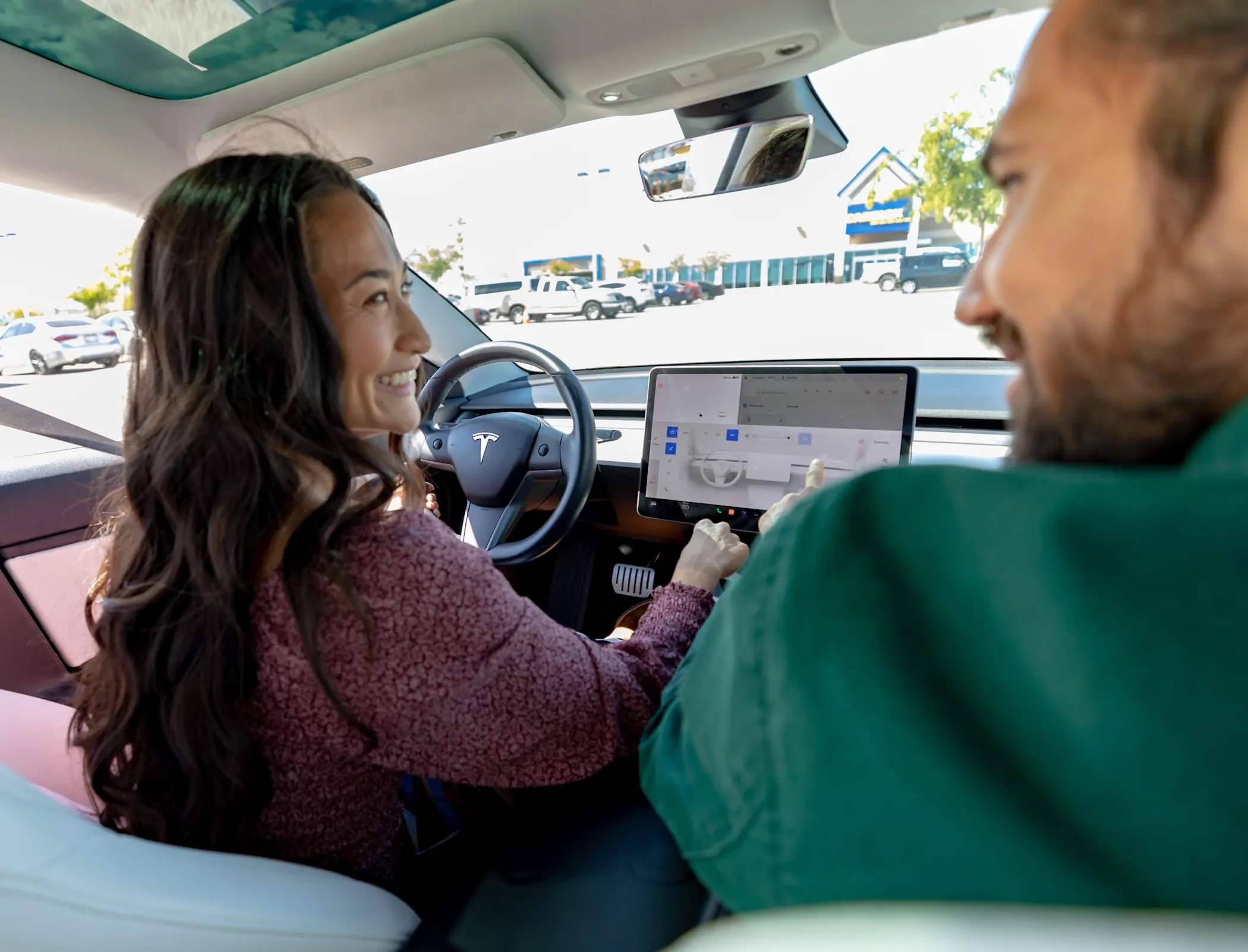 Woman in driver's seat smiling at man in passenger seat while she interacts with digital console