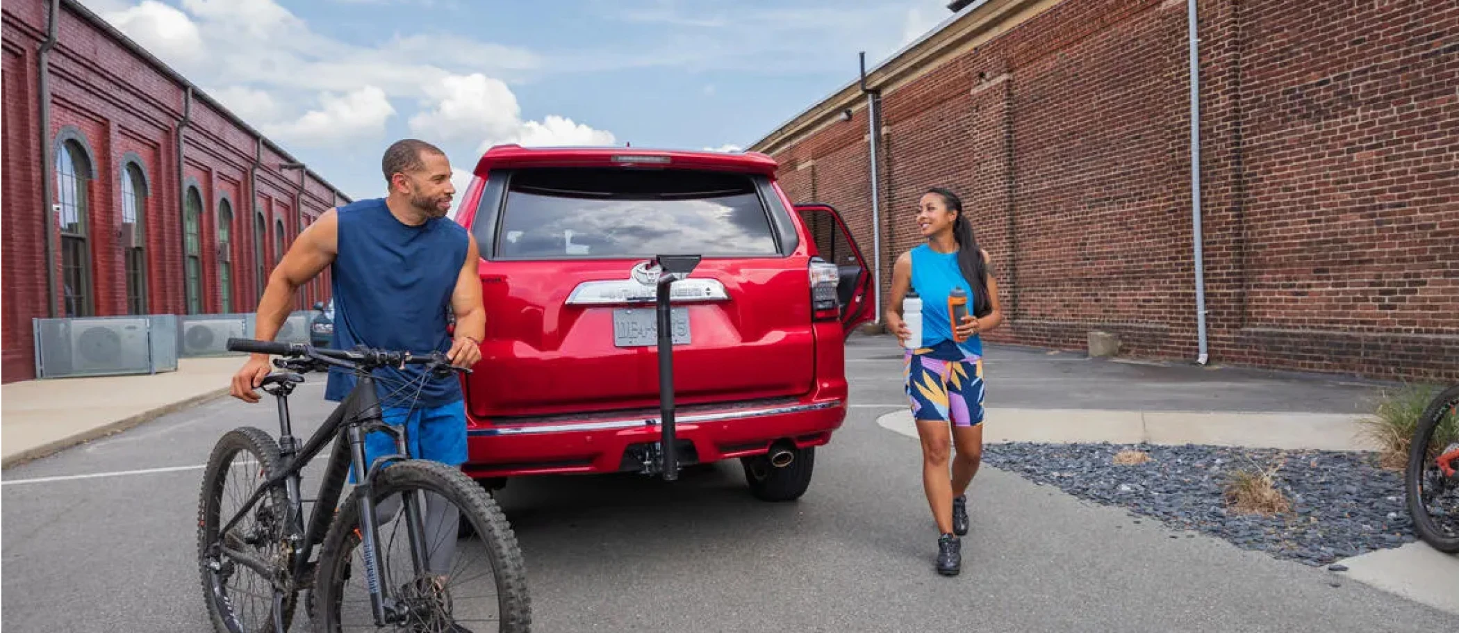 Man with bicycle behind SUV with bike rack