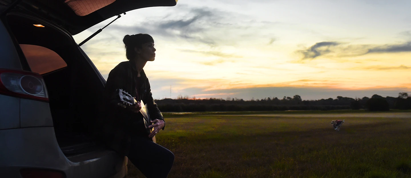 Person resting on SUV playing guitar at sunrise 