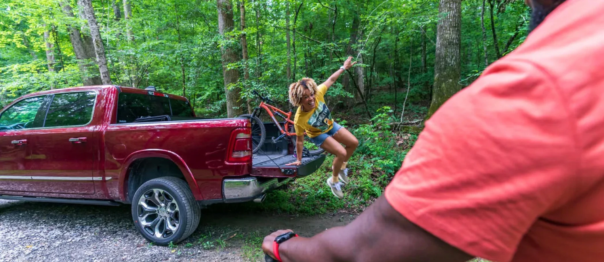 Woman jumping from back of truckbed. Man on a mountain bike in the foreground