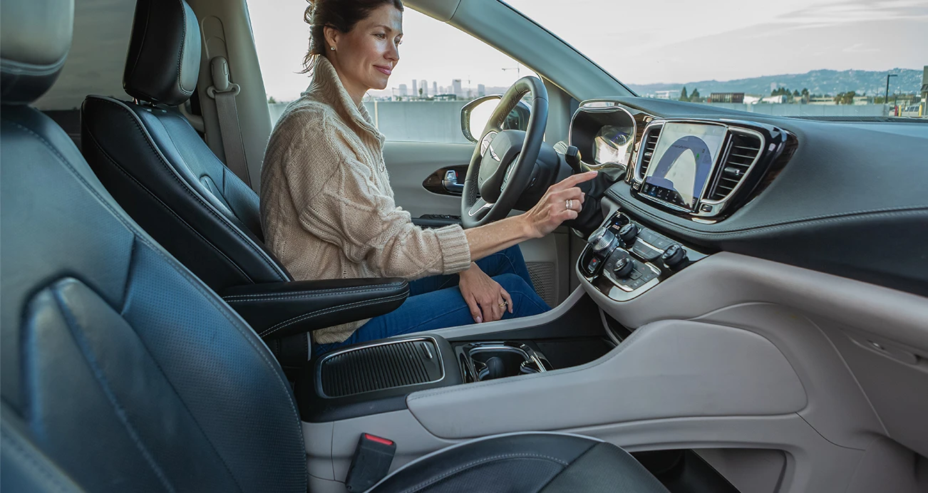 Host sits in drivers seat of a Chrysler Pacifica and makes selection on infotainment screen