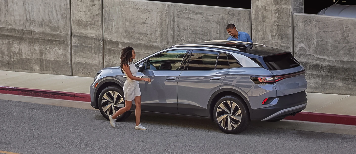 Woman and man energetically jumping into a silver luxury SUV parked on a city street