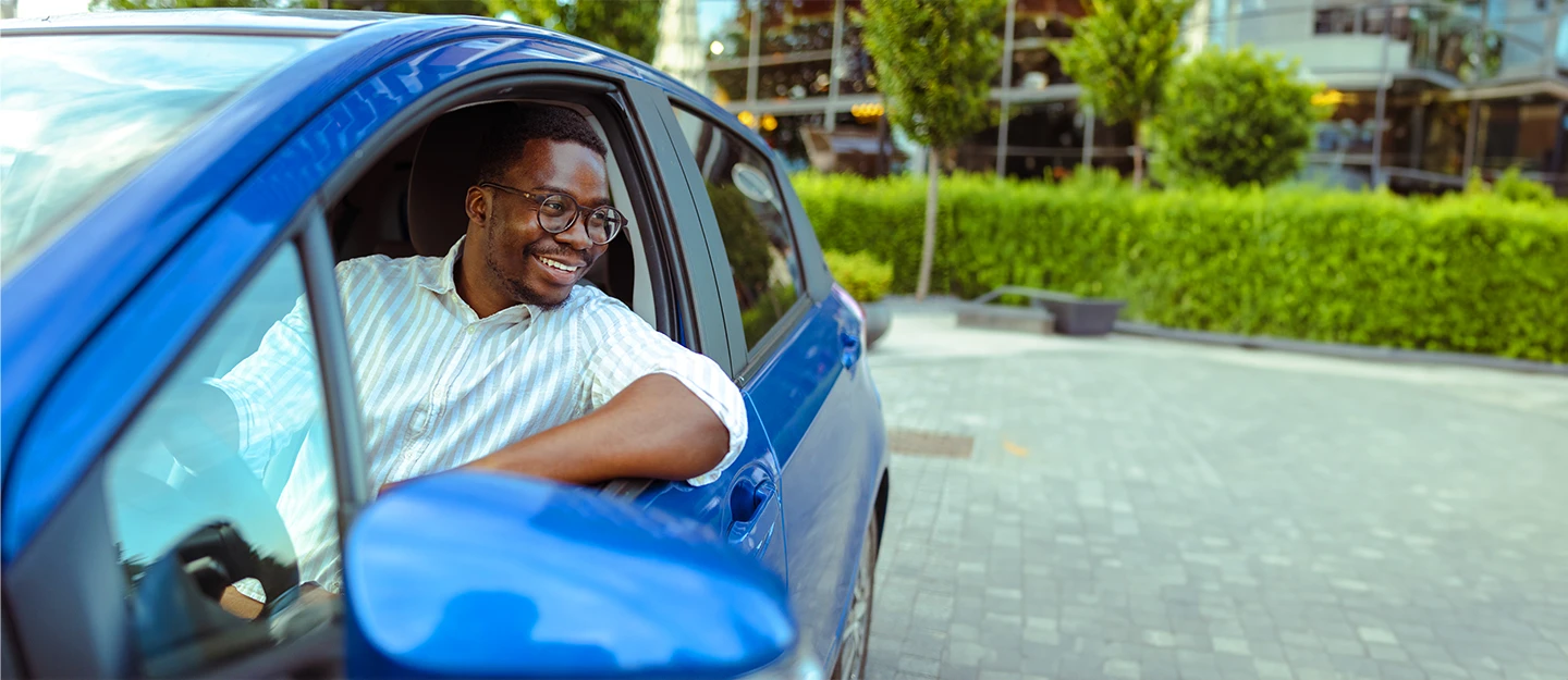 Man smiling while driving with the window down in his blue car.