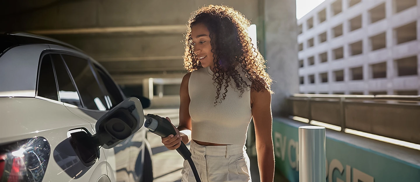 Woman in white shirt plugs white vehicle into fast charging station