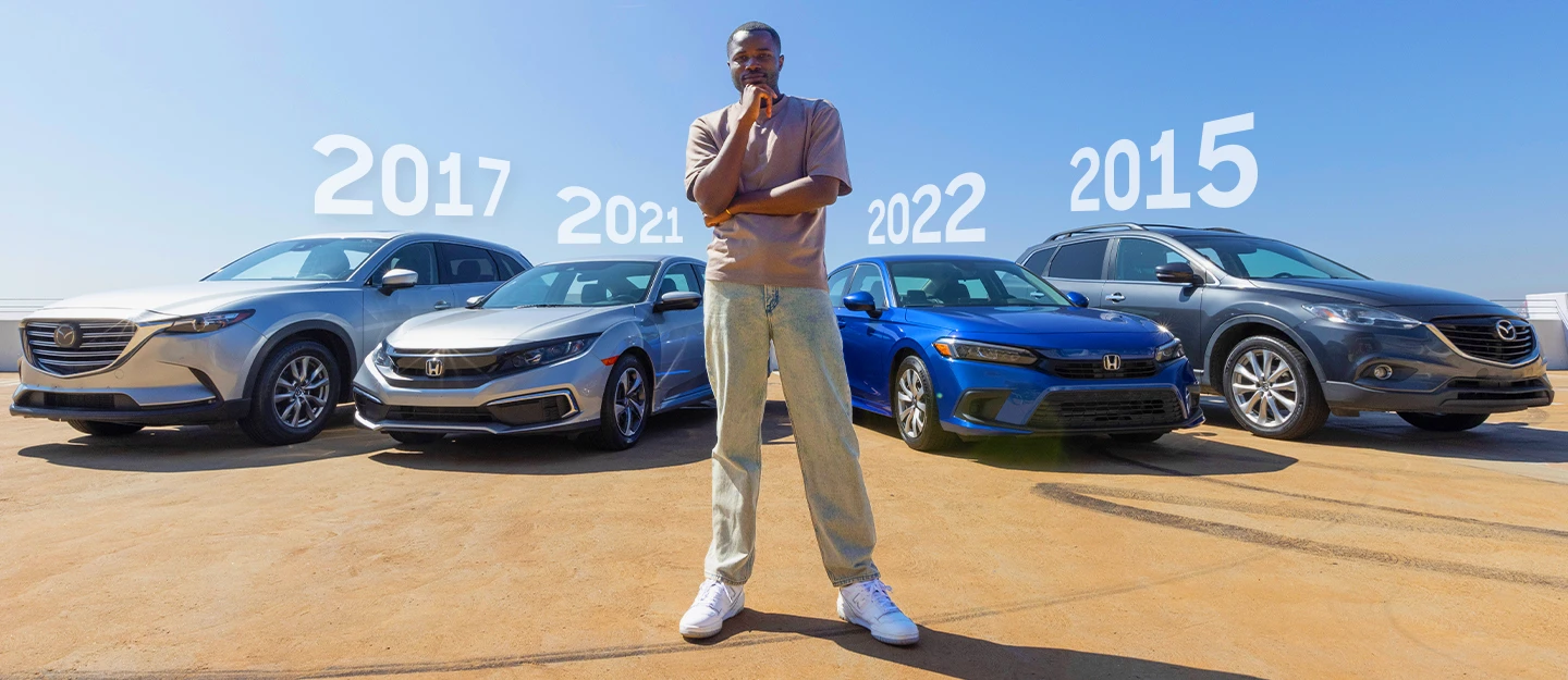 Man standing in thinking pose in front of a silver 2017 Mazda CX9, a silver 2022 Honda Civic, a blue 2021 Honda Civic, and a dark pewter 2015 Mazda CX9