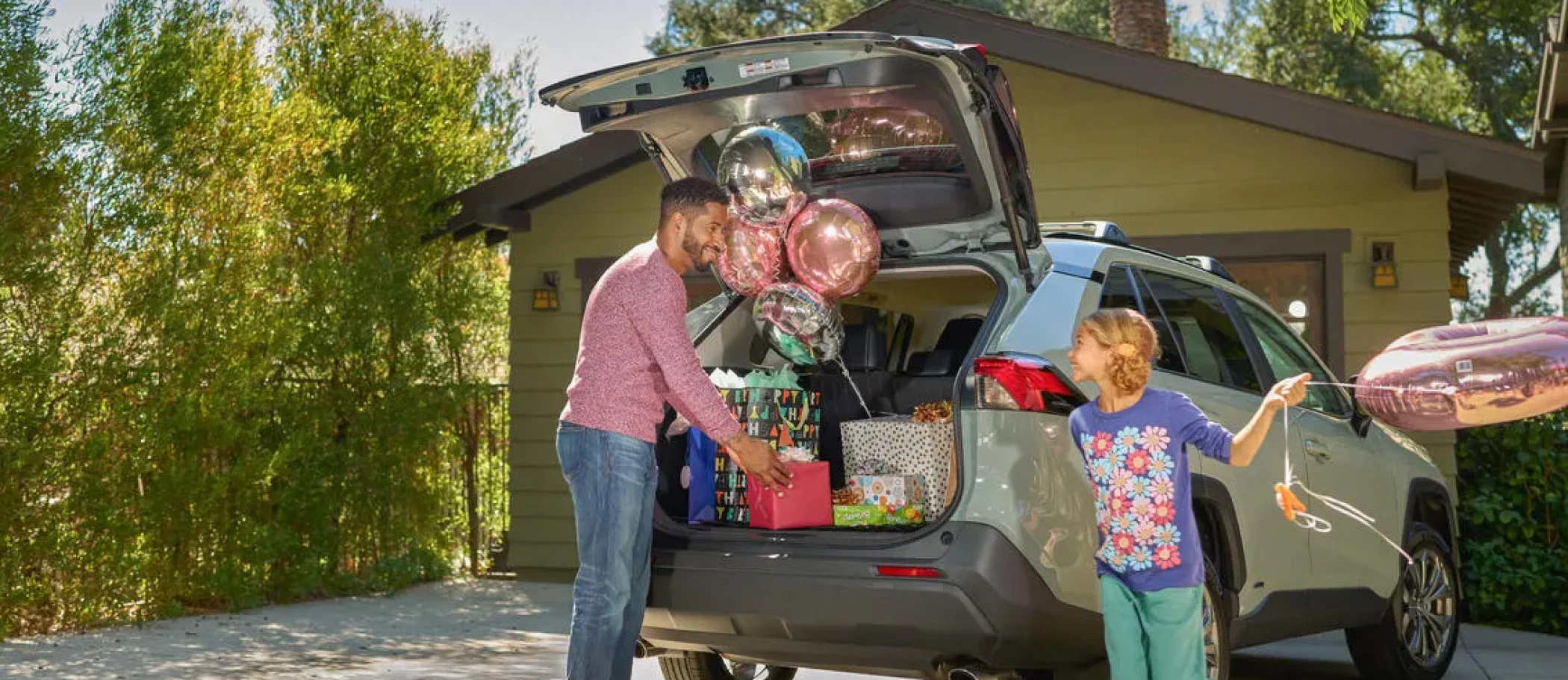 A man and a girl unpacking birthday presents and balloons out of the back of an SUV