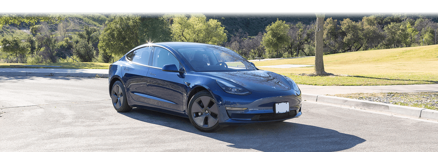 Blue Tesla Model 3 parked next to grassy area