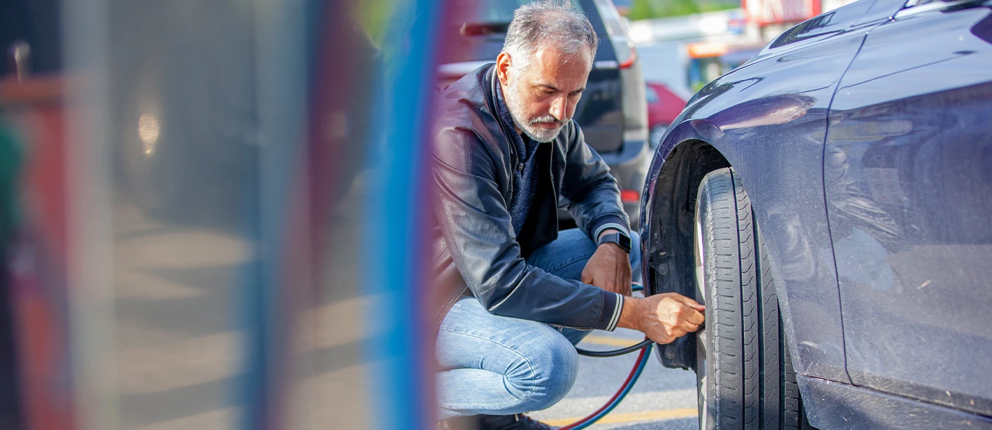 man kneeling by the front wheel of his car checking the tire