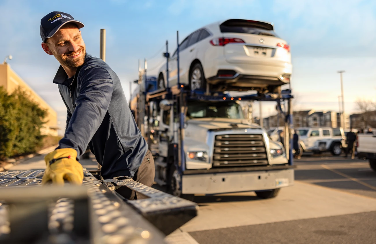 CarMax store associate wearing gloves and a cap smiling as he assists with a truck to ship used cars