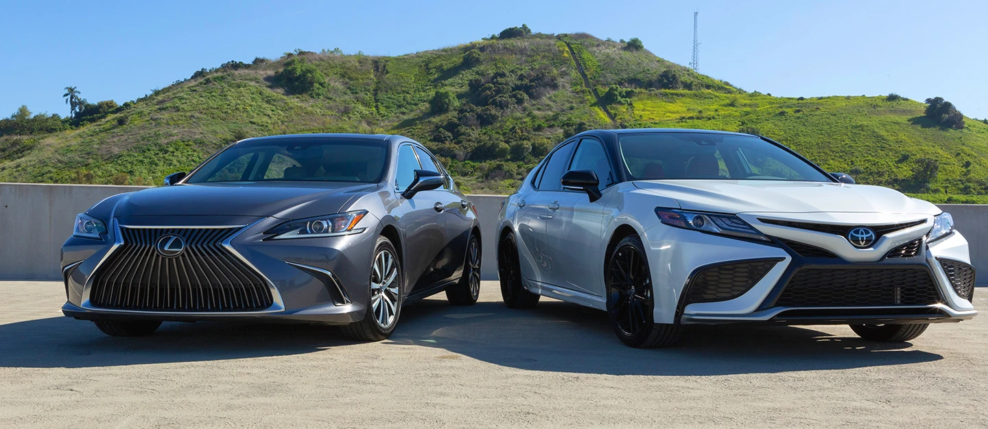 2020 Lexus ES 350 and 2024 Toyota Camry parked side by side blue sky and grass hill behind