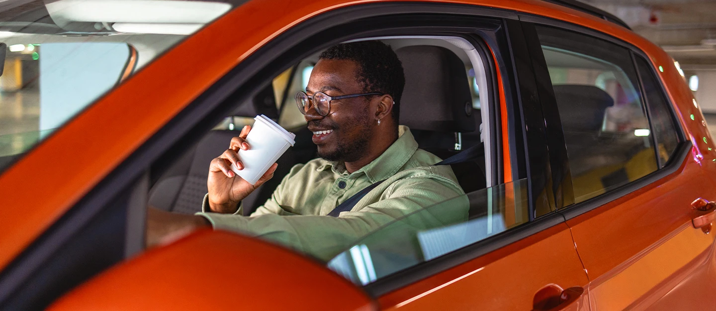 Man sipping coffee in the drivers seat of an orange compact car