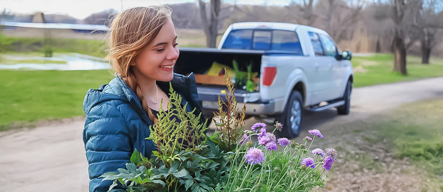 Young girl holding a bunch of wildflowers, with a midsize white truck parked in the background along a quiet country road.