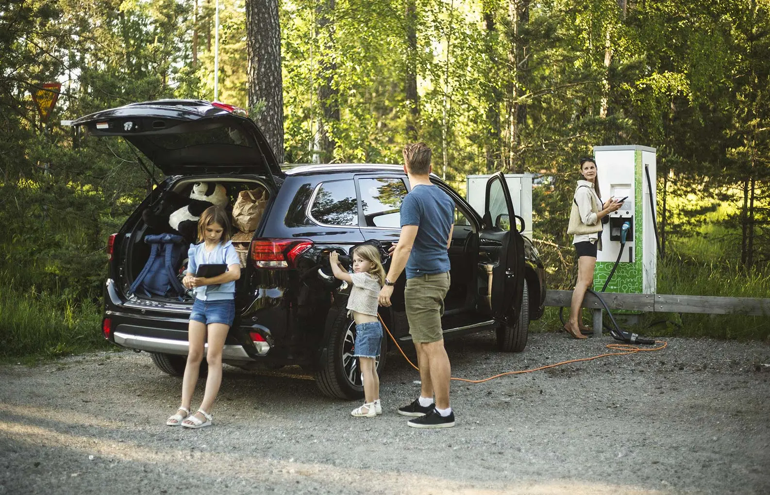 Family at a charging station charging their EV with forest in the background