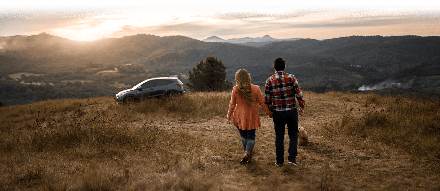 Couple walking towards SUV as sun sets on mountains 