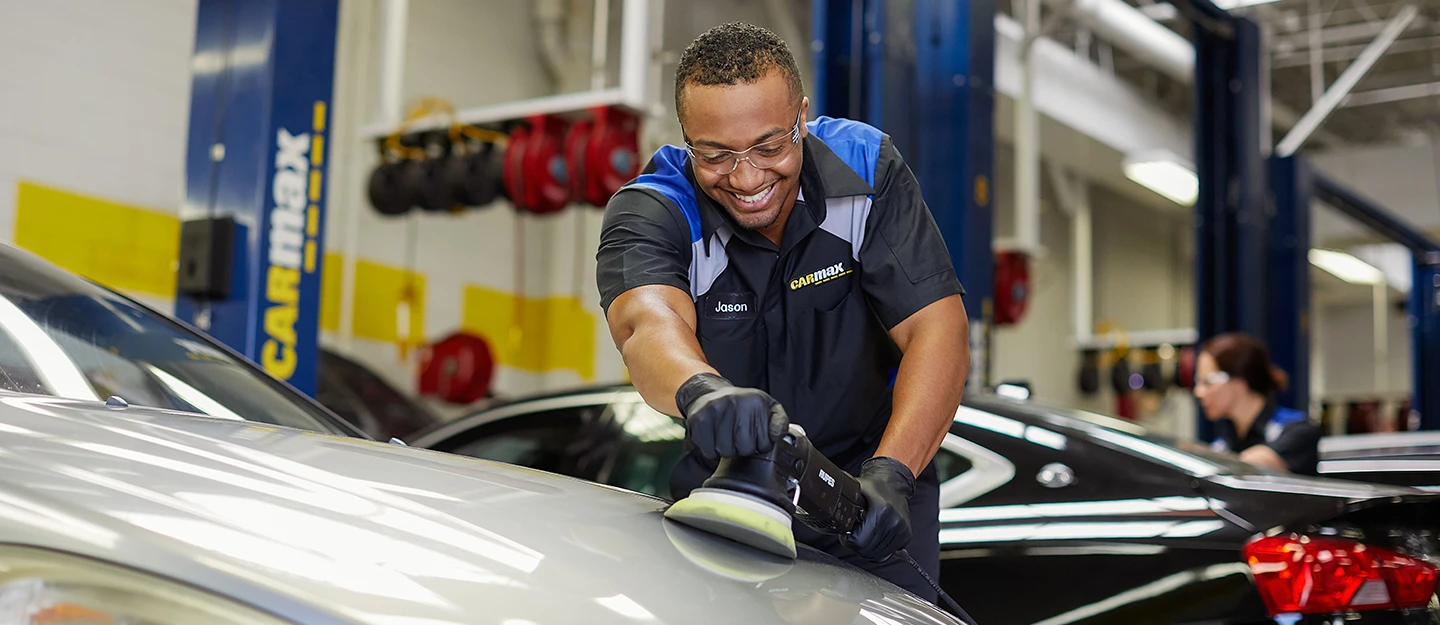 CarMax Auto Technician smiling while he works on detailing a vehicle in the shop preparing the car to sell
