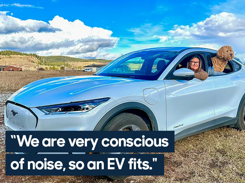 A woman sits in the drivers seat of a Ford Mustang Mach E with her elbow leaning on the open window. A brown curly-haired dog sticks their head out of the back driver-side window. Text overlaid on the image reads "We are very conscious of noise, so an EV fits."