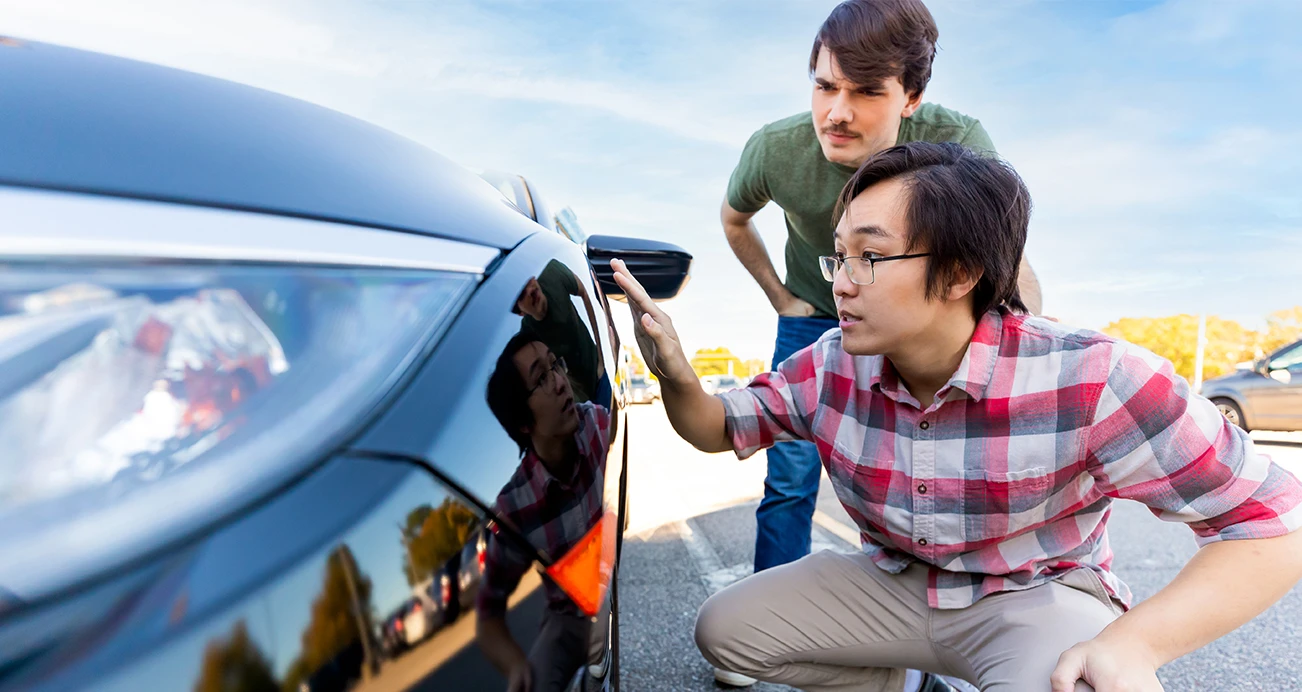 Two friend kneeling at the fron of a black sedan inspecting the vehicle before taking it on a test drive