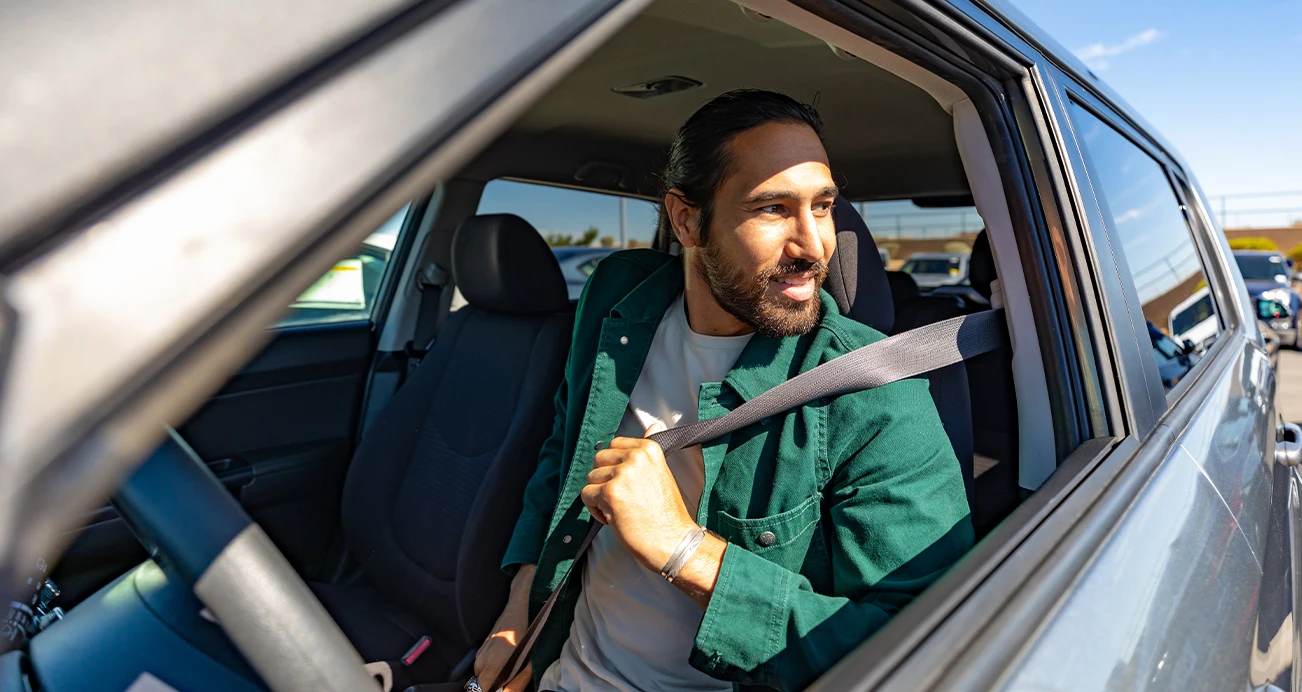 Man sitting in drivers seat buckling up his seatbelt while looking out the window 