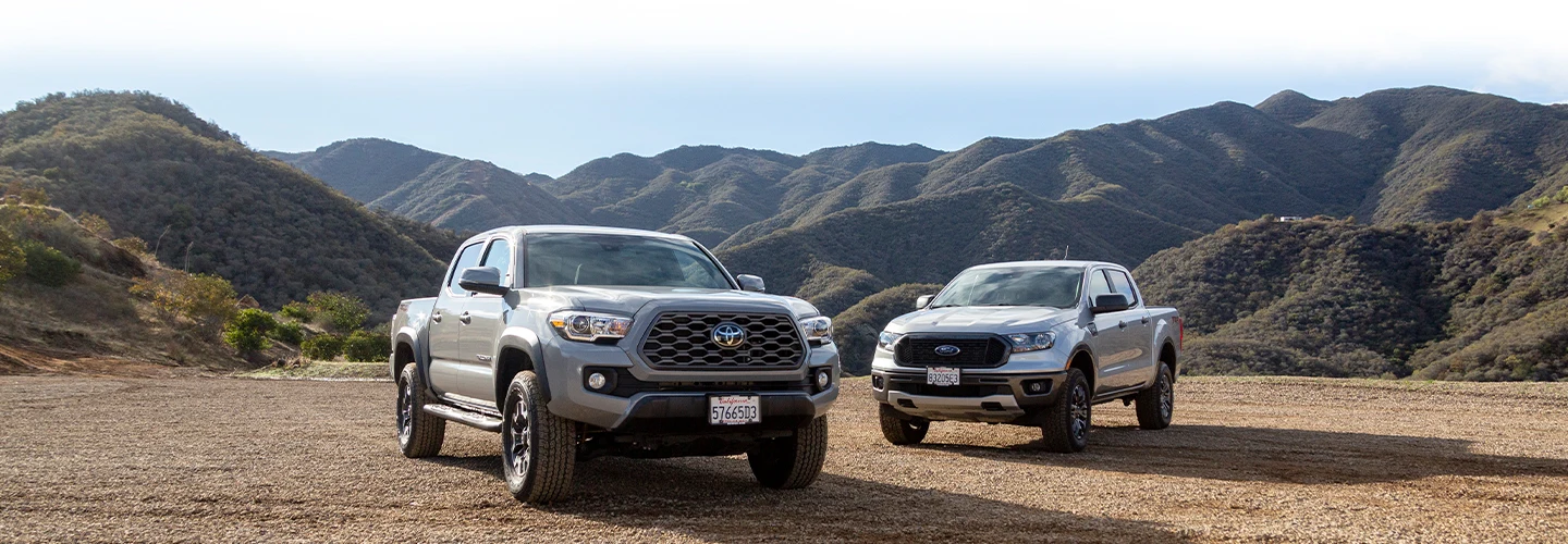 A silver Toyota and silver Tacoma Ford Ranger parked in front of moutain range