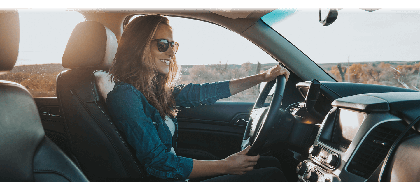 Woman with sunglasses on sitting in drivers seat with both hands on steering wheel