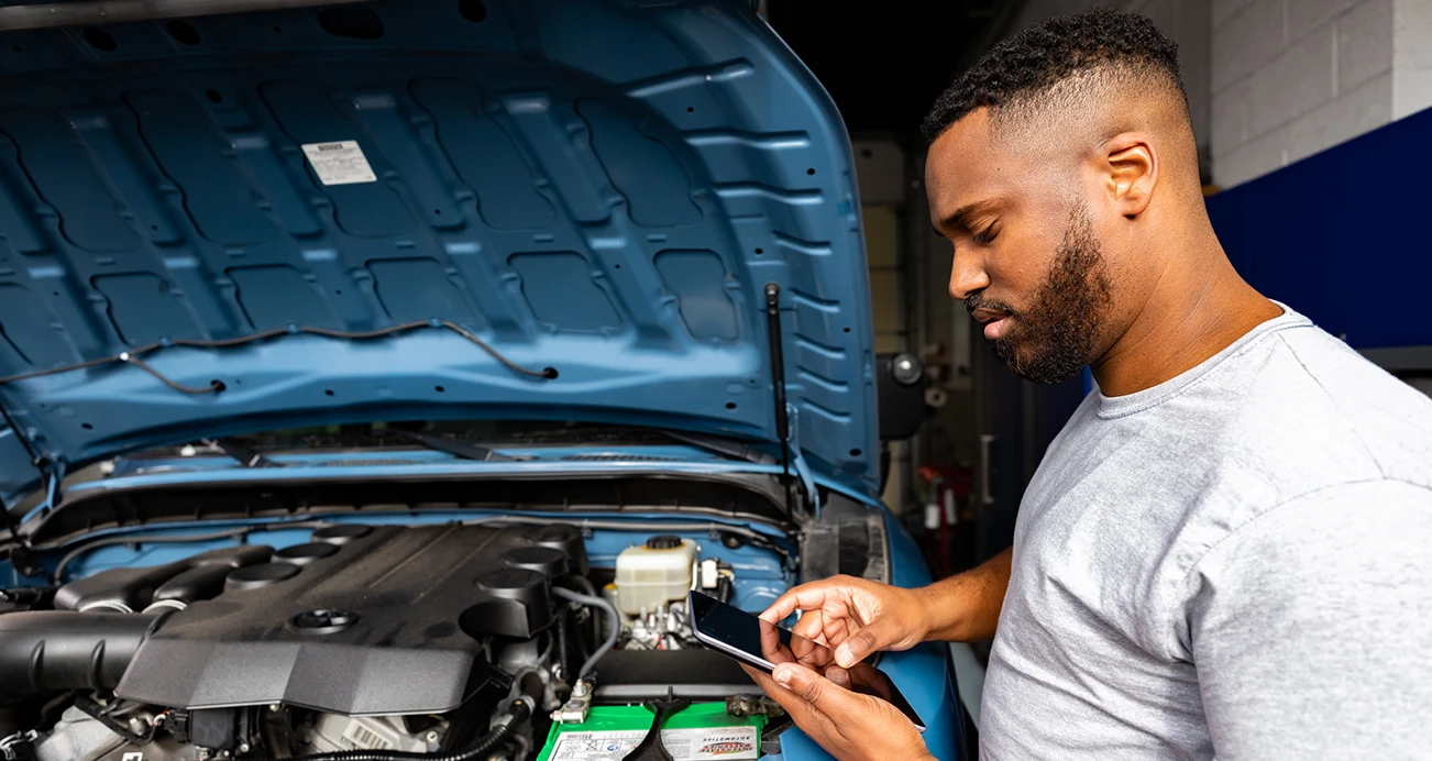 Man searching on phone while looking under the hood of his car 