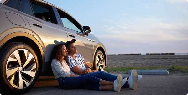 Can an EV fit my lifestyle? Image of two people sitting on the ground watching the sunset with their backs leaned against an electric vehicle