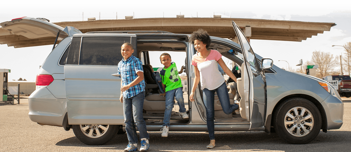 Children smiling getting out of silver minivan 