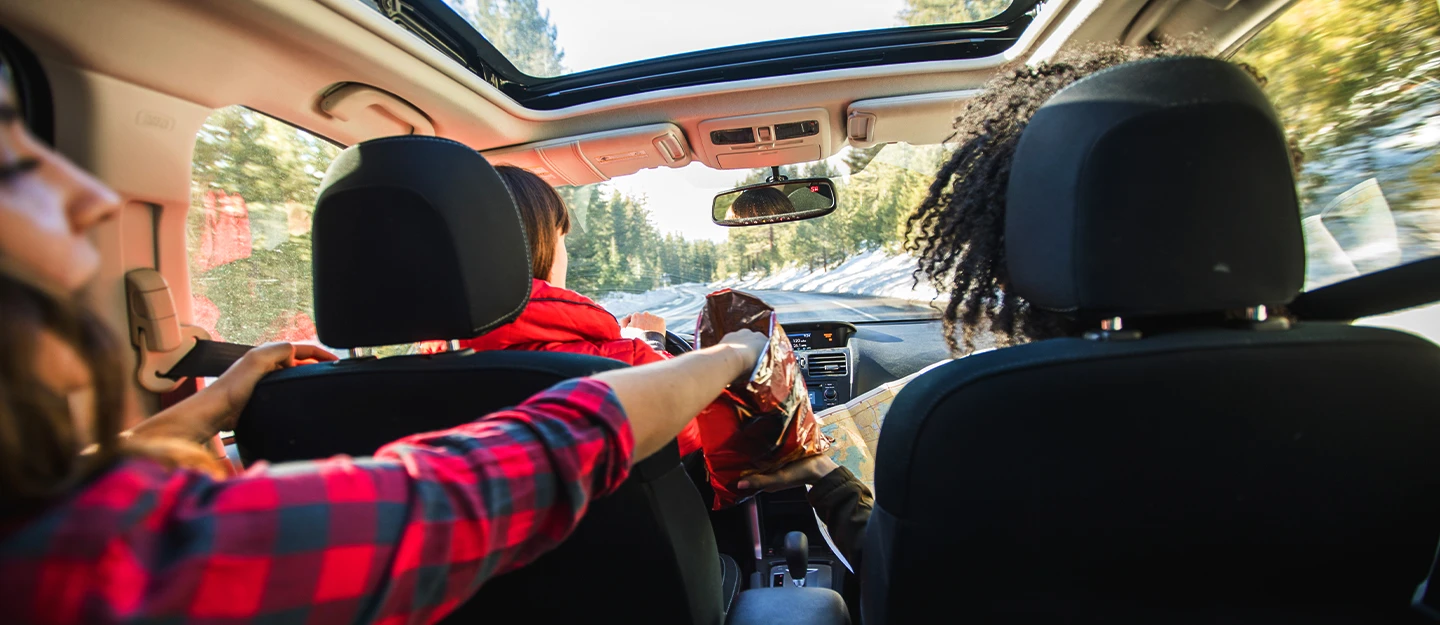 3 friends road tripping and eating snacks in their SUV. The sun roof is open 