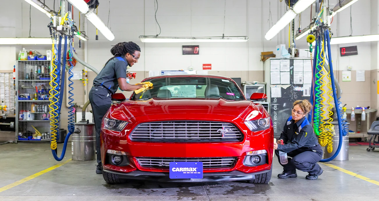 Two mechanics working on a red Ford Mustang in a shop 