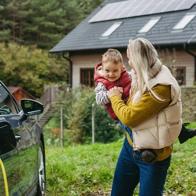 Mother holding smiling toddler walking toward her plug-in-hybrid as it charges