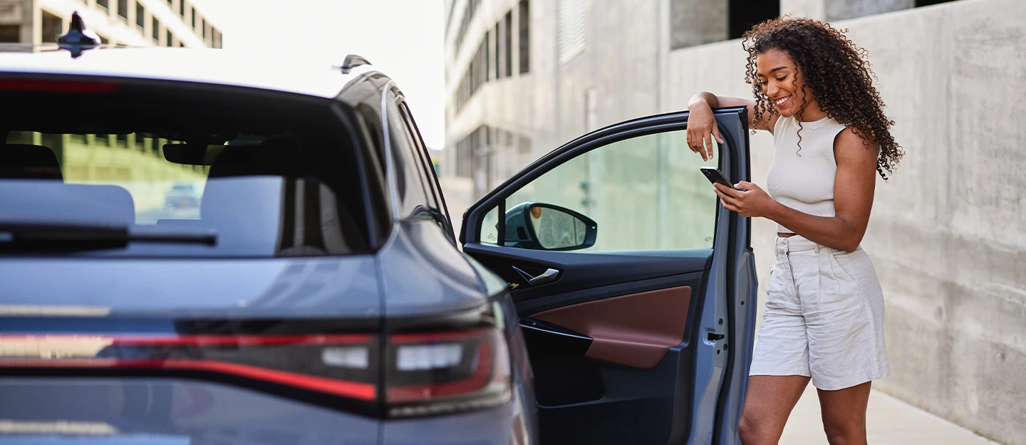 Woman look at her phone smiling as she opens the driver seat of her luxury car 