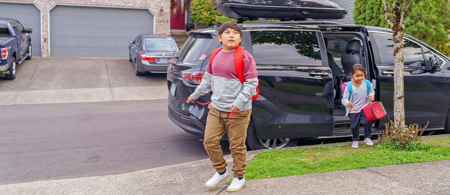 Brother and sister walking out of their black minivan with backpacks on