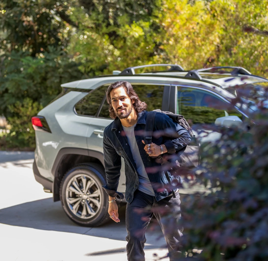 Man walking away from SUV towards the camera with a bush in the foreground