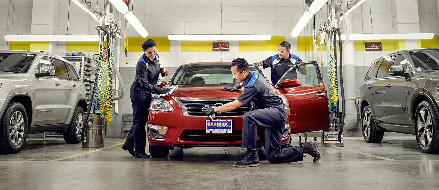Three service technicians working on a red sedan in a CarMax service center 