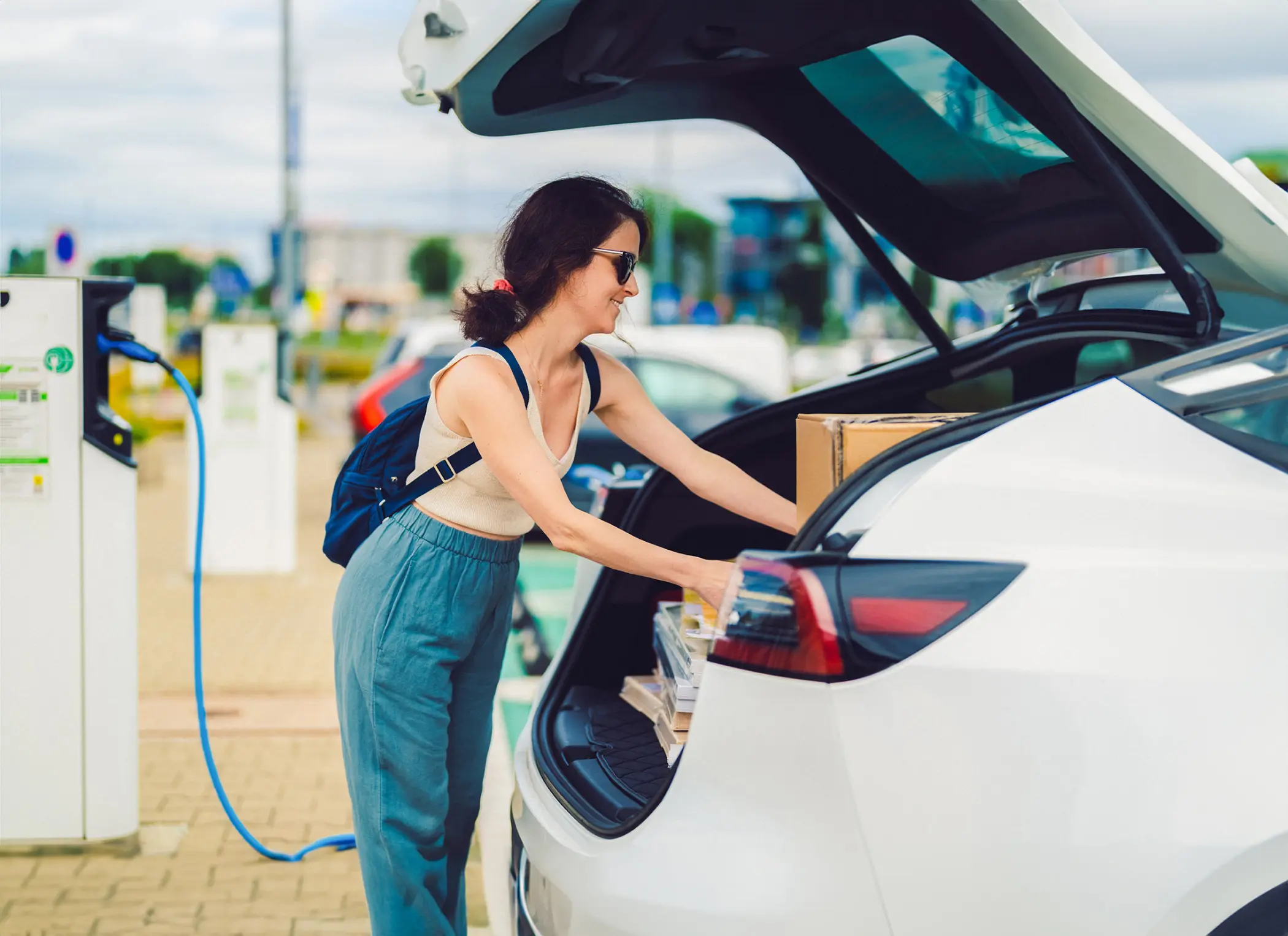 Woman at a charging station loading items into back of SUV