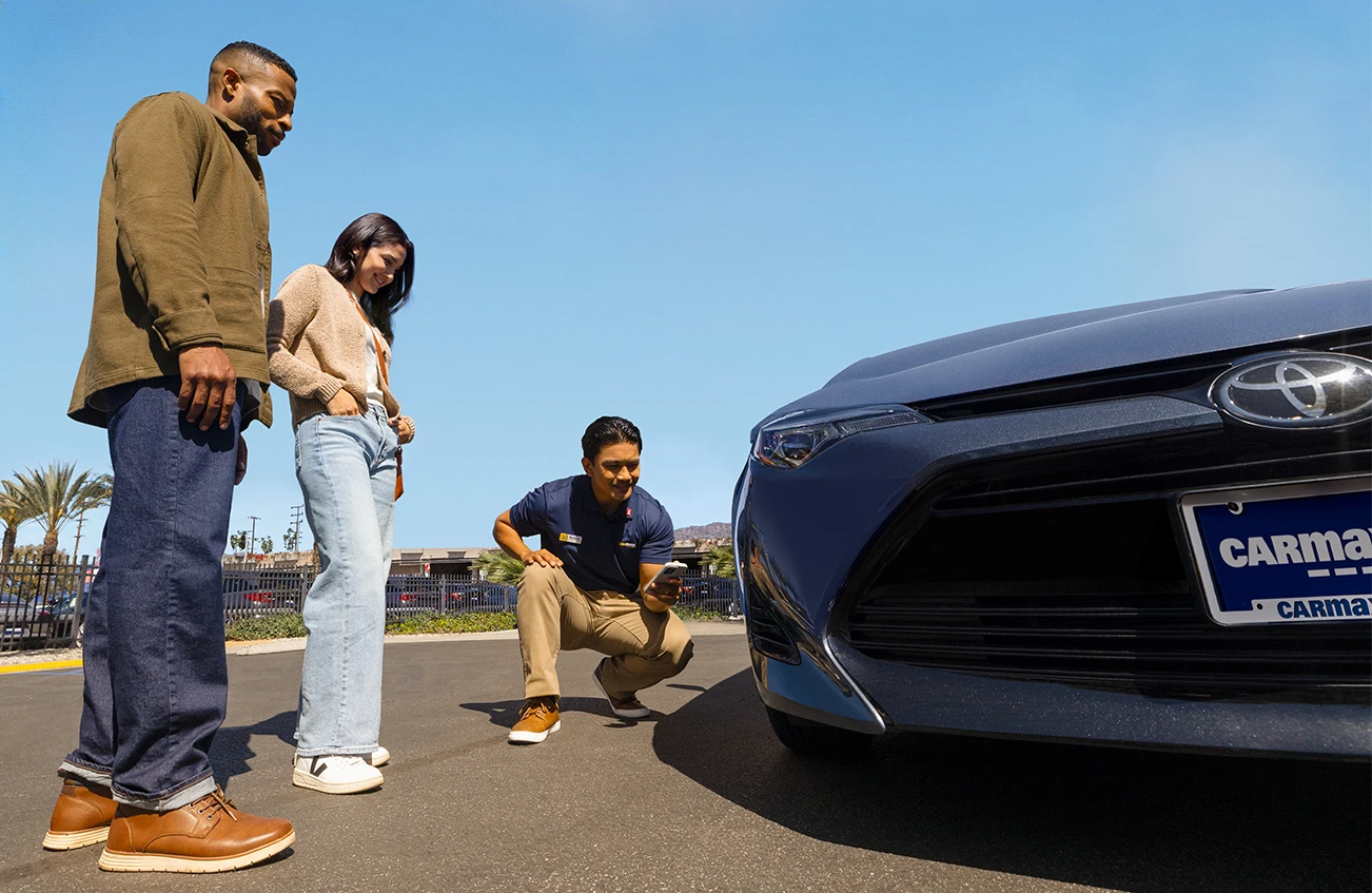 Store associate motions to white toyota RAV4 on the lot at a CarMax store location